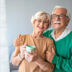 Happy,senior,man,embracing,woman,in,front,of,windows,at